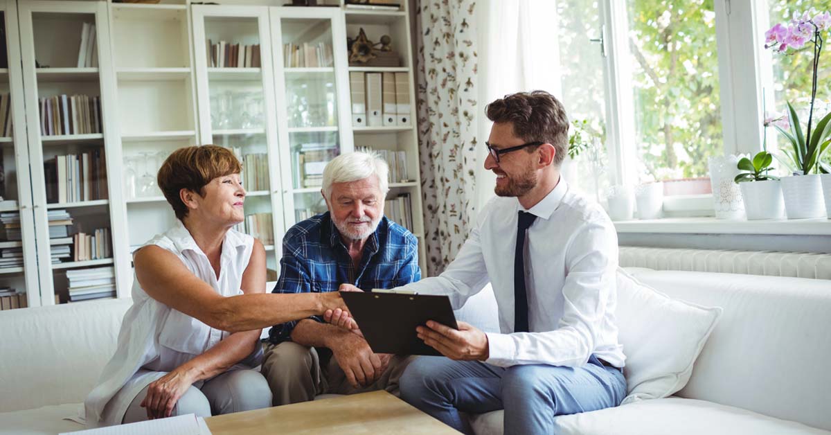 Ein älteres Ehepaar sitzt in seinem Wohnzimmer und bespricht mit einem Immobilienmakler Lösungen für seine Immobilie und wie man davon im Alter profitieren kann | Wohnen im Alter